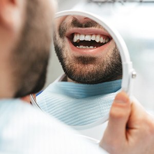 Man smiling at reflection in handheld mirror