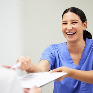 Smiling dental assistant handing patient form