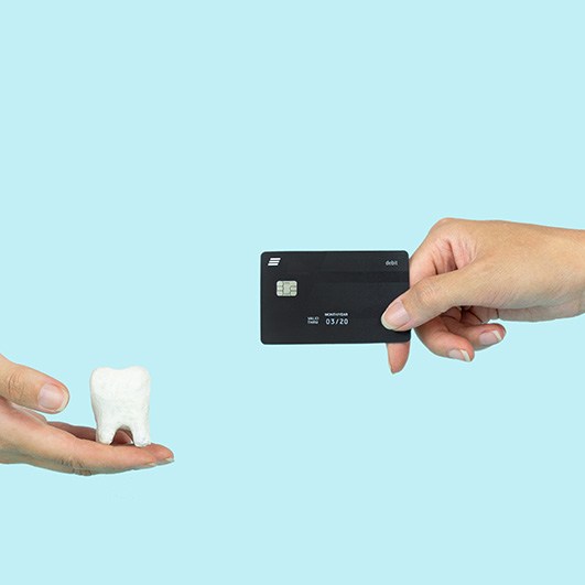 Hand holding out black credit card to another hand holding out model tooth