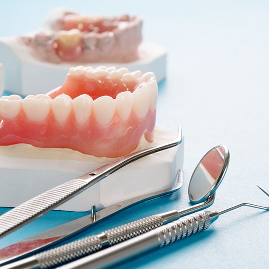 Model of denture next to dental tools