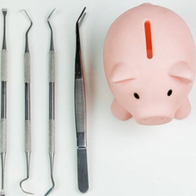 Dental tools next to a piggy bank on white background