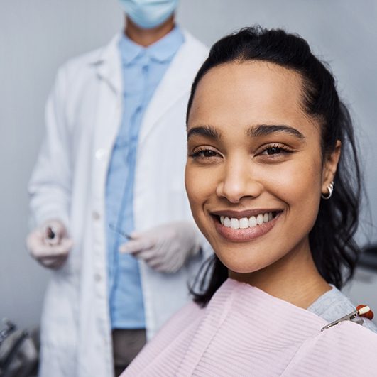 Woman in dental chair smiling with dentist behind her in background