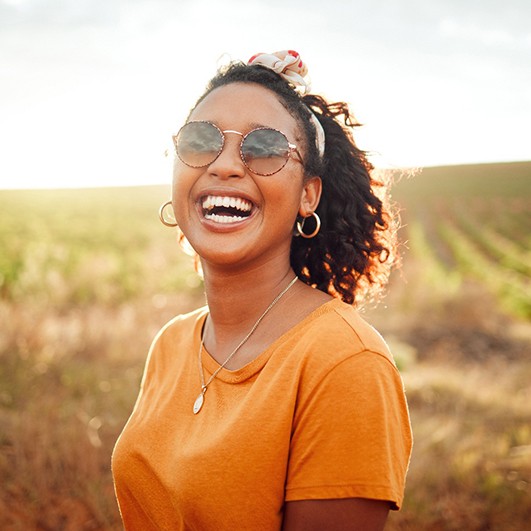 Woman in orange shirt and sunglasses outside in field smiling