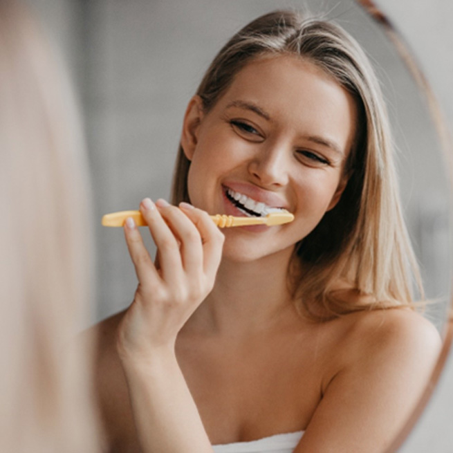 Young woman brushing her teeth in front of bathroom mirror