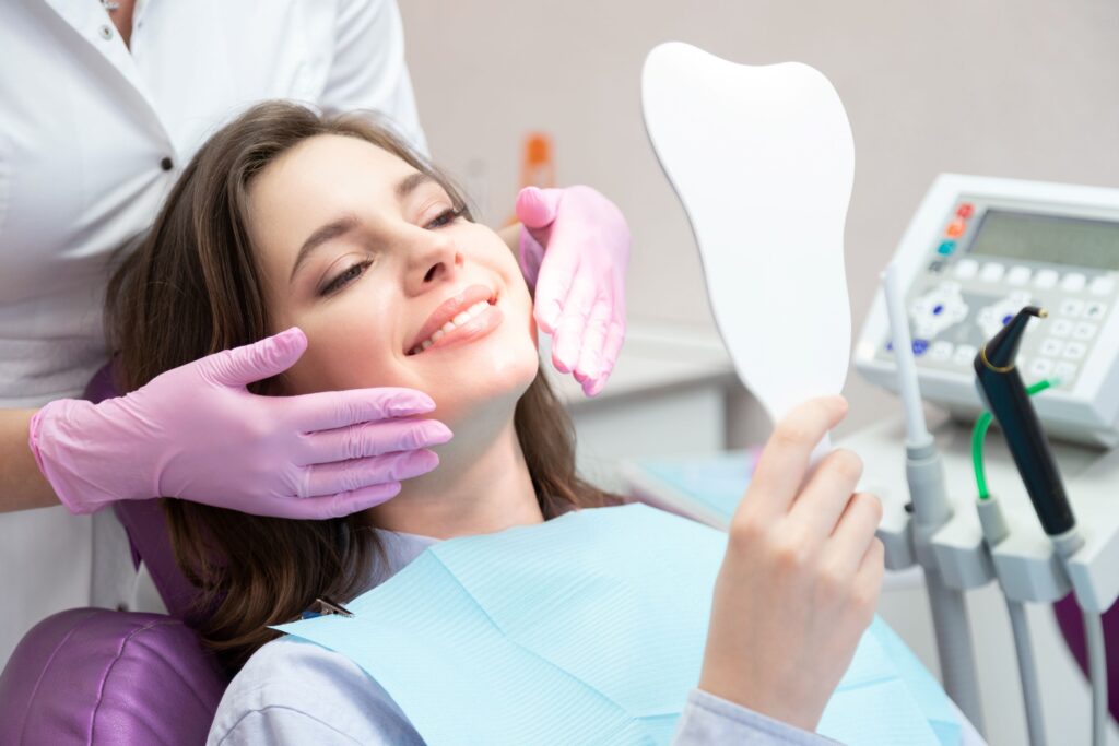 Woman in dental chair smiling into mirror with dentist's hands by her face