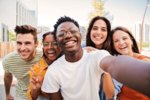 Group of young adults smiling and taking selfie together outside